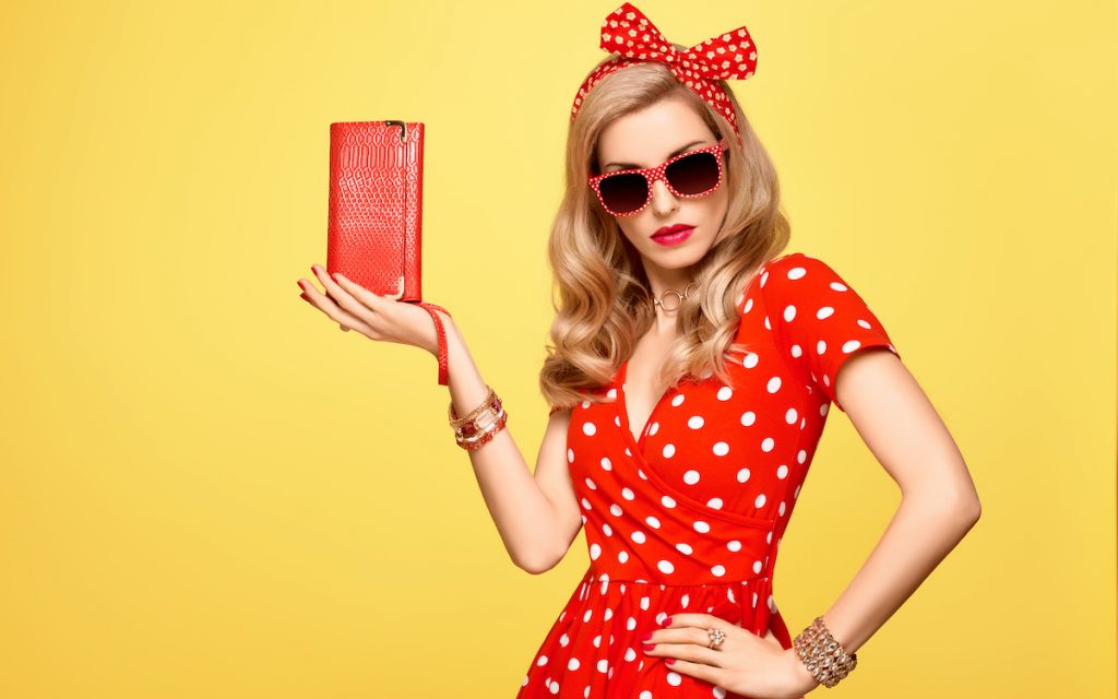 woman wearing red polka dot dress with matching polka dots headband and holding a red purse